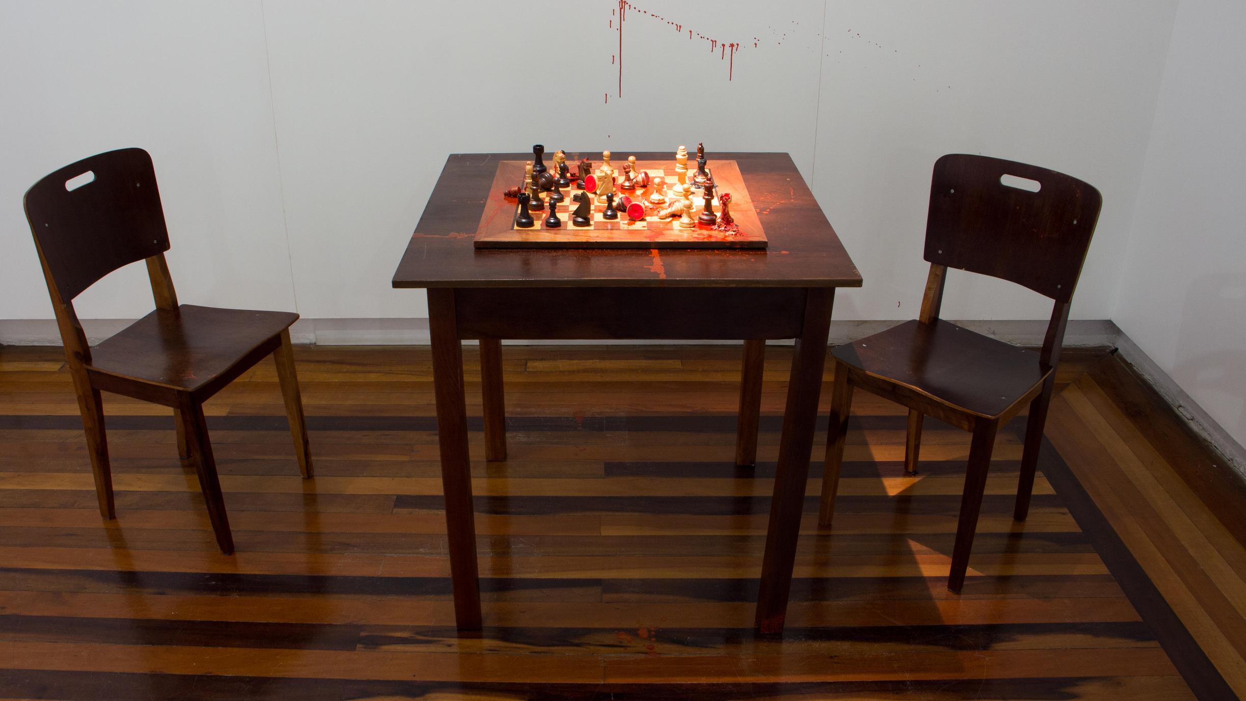 Xeque-mate, Cyntia Werner, 2015. Instalação, mesa, cadeiras e intervenção sobre tabuleiro de xadrez, aproximadamente  100x200cm.